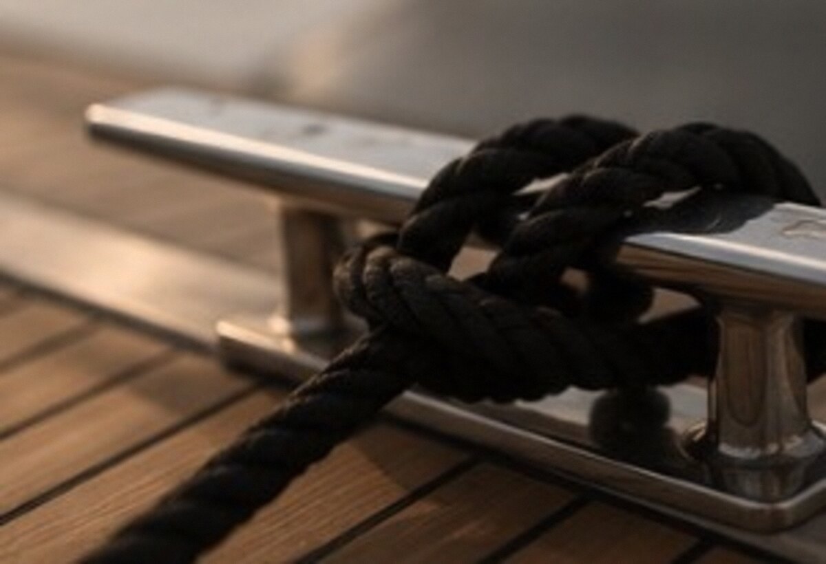 Polished stainless deck cleat and coiled line on warm teak decking